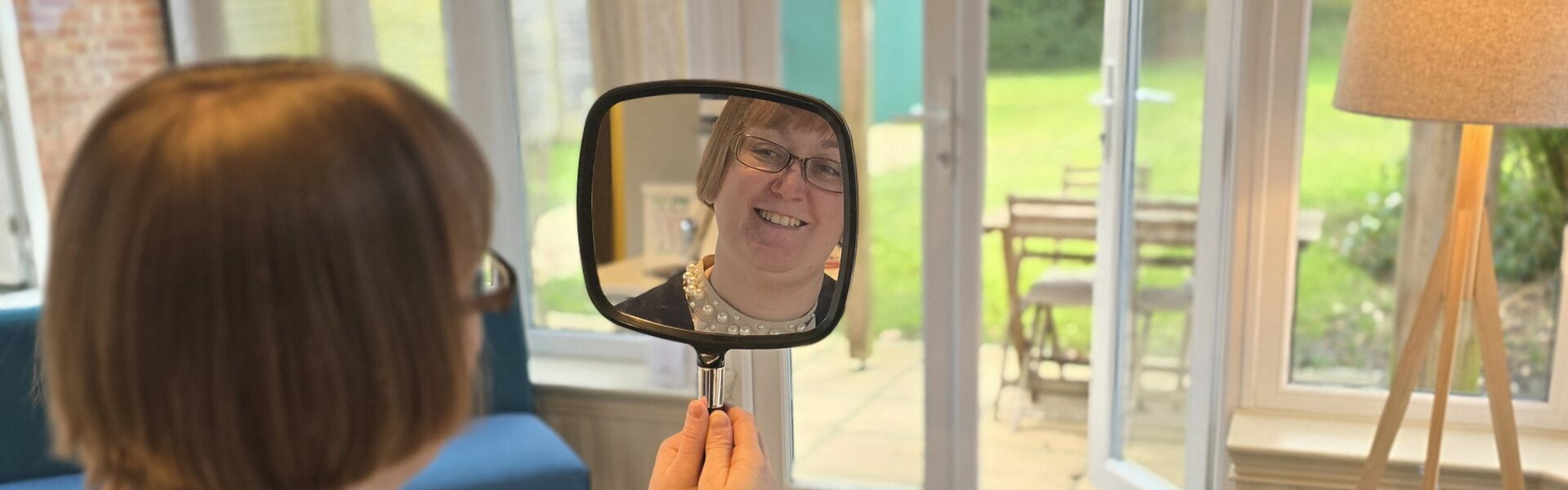 Invisalign patient at Park Lane Orthodontics smiling at her new smile in a hand mirror